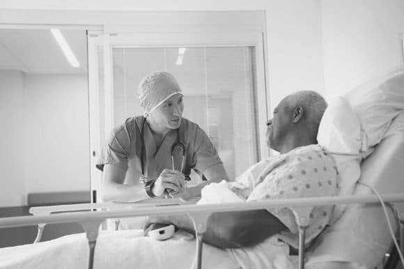 A hospital attendant comforts a patient who is lying in a hospital bed.