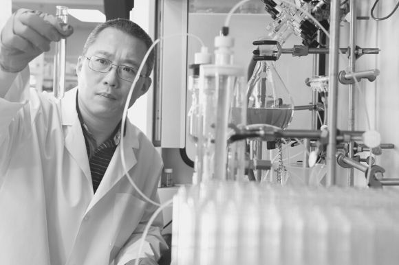 A laboratory technician, holding a beaker, examines a sample in the lab.