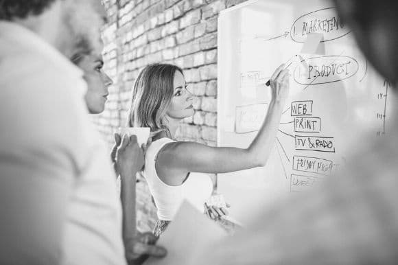 A public relations manager works out a client's strategy, with colleagues, on the white board.