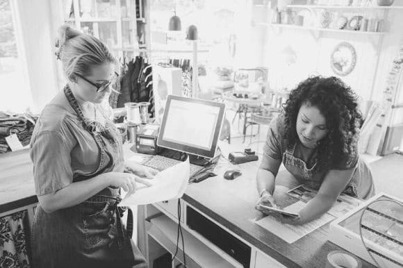 Two retail store colleagues checking records and discussing inventory.