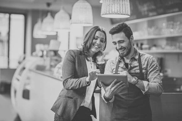 Restaurant general manager and kitchen manager discussing inventory, looking at a tablet computer.