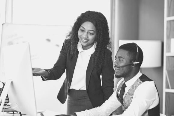 Sales trainee working on computer with trainer in office