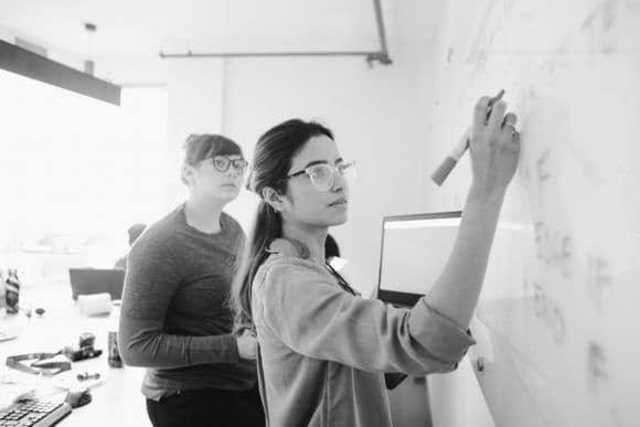 Two software developers working on code on a white board.