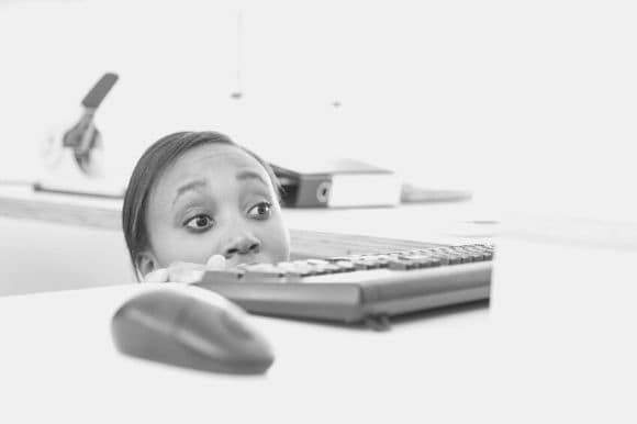 A visibly frightened woman hides behind her desk to stay safe during an incident of workplace violence.