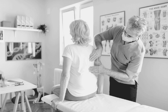 Chiropractor making adjustments to a patient's back as they sit on the edge of the exam table.