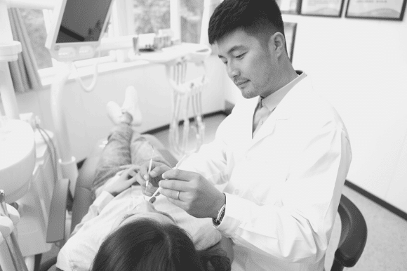 Dentist standing next to a patient and checking her teeth.