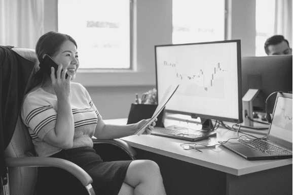 Economist sitting at desk, reviewing financial data, and discussing it with a colleague on the telephone.