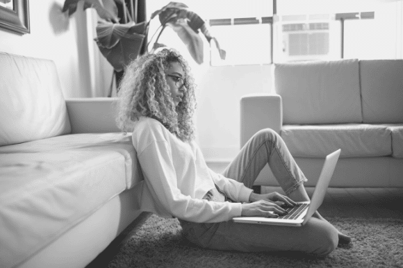 Woman working on a laptop while reclining on her living room floor, highlighting hiring best practices for remote workers.