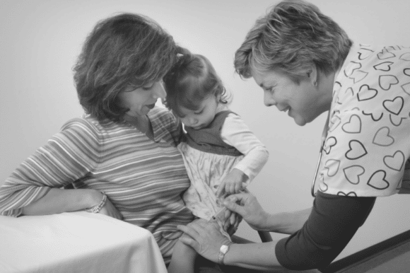 Pediatric nurse giving an injection to a toddler sitting on her mother's lap.